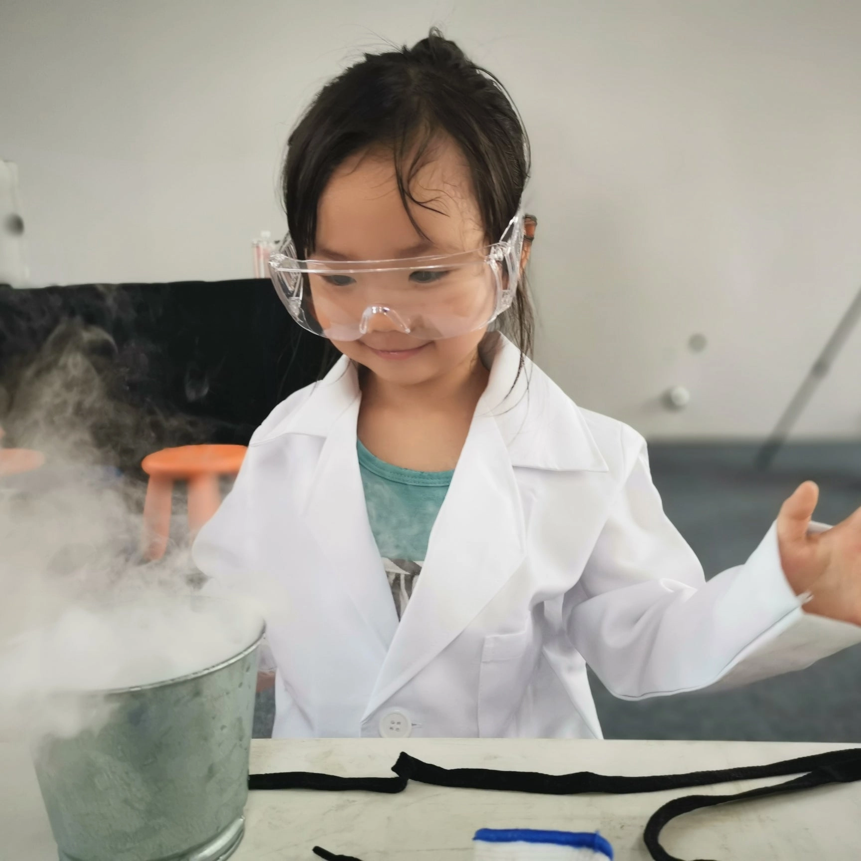 Young girl in a lab coat and safety goggles with a smoking experiment