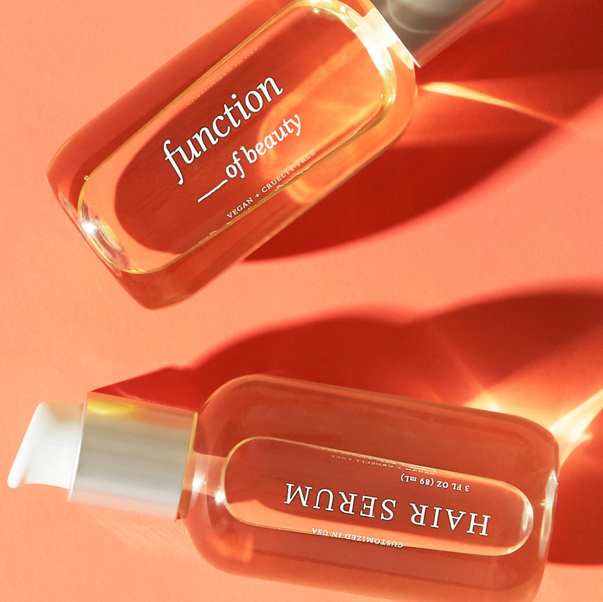 Two orange bottles of hair serum on a coral background