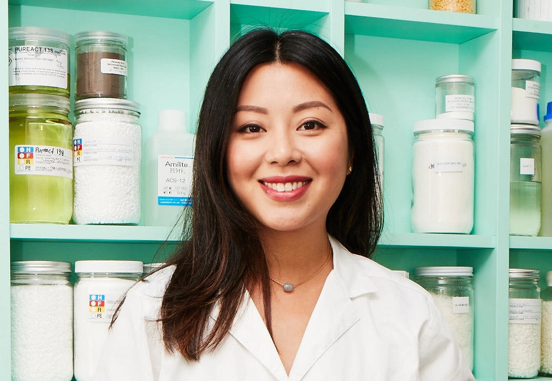 Hien Kaplan smiling in a lab with shelves of ingredient jars