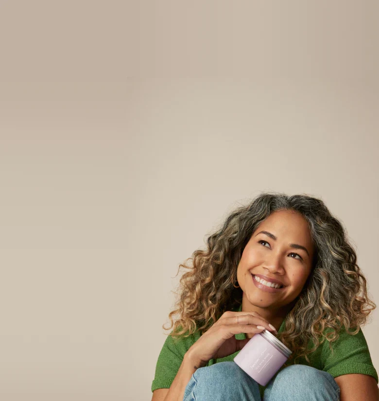 Smiling person with curly hair holding a jar of hair mask